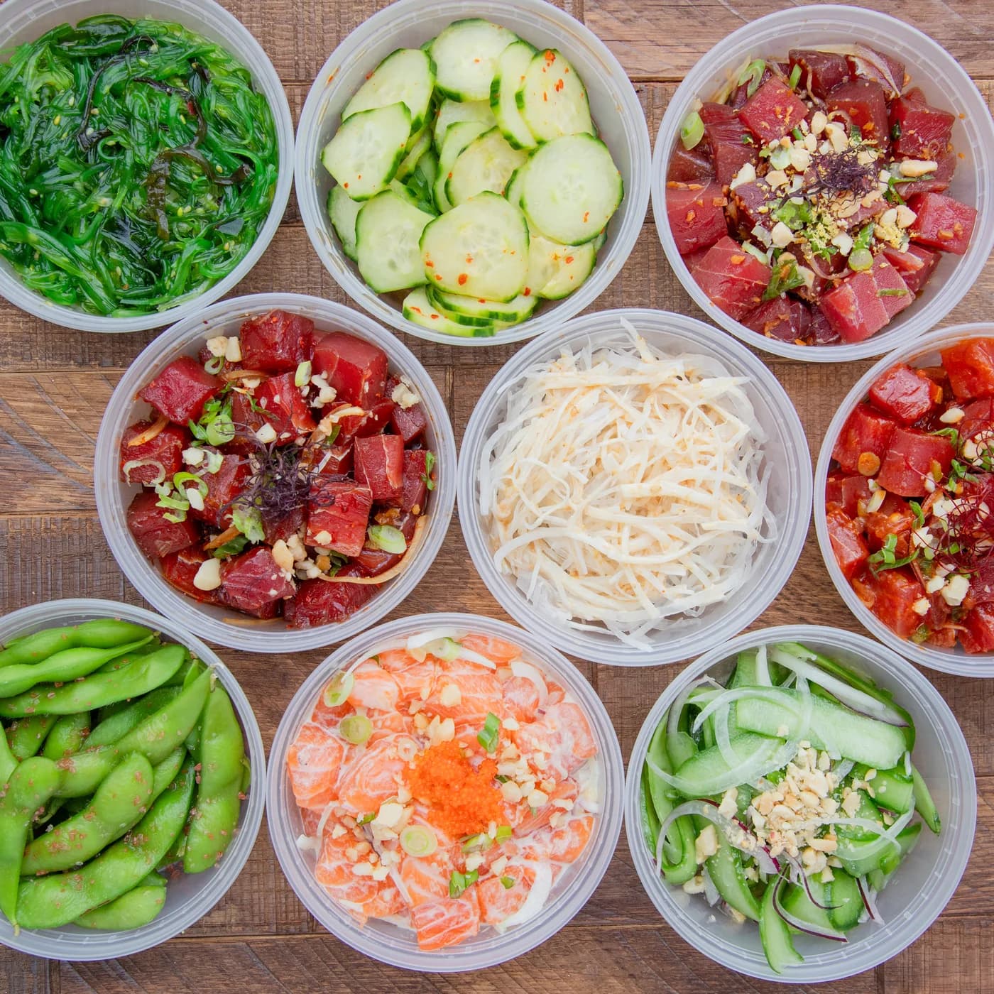 Overhead spread of tuna and salmon poke with seaweed salad, cucumber salad, edamame, and crab salad